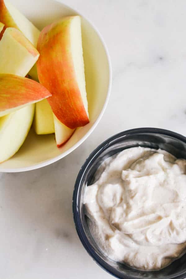 Cinnamon vanilla Greek yogurt apple dip in a black bowl on a marble countertop next to apple wedges.