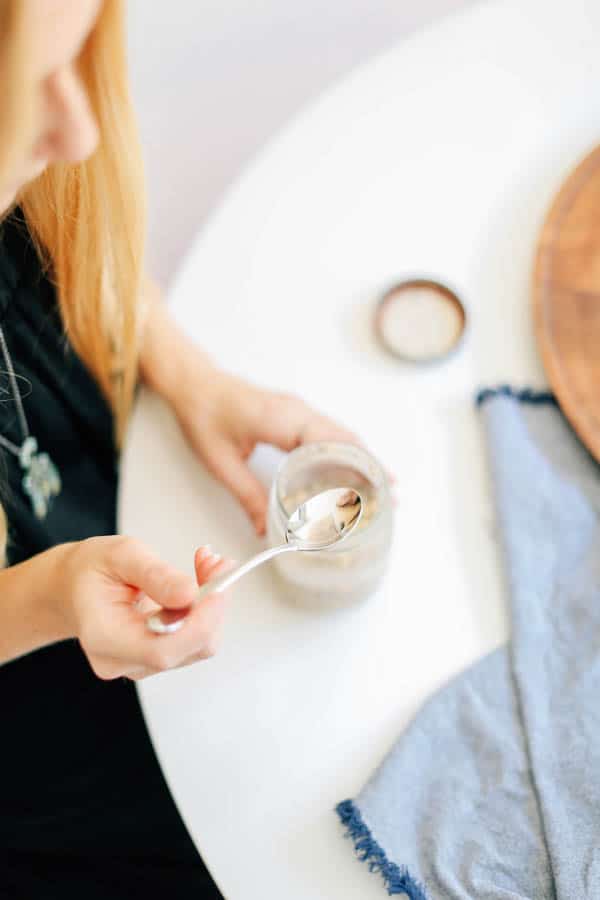 A woman sitting at a white table getting ready to eat a jar of overnight oats.