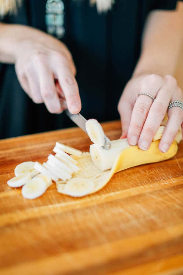 A woman slicing a banana on a wooden cutting board.