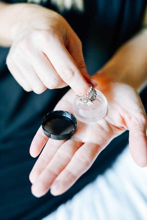 Woman putting wedding rings in a small plastic container to keep it safe on vacation. 