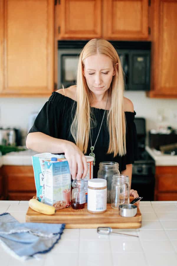 A woman arranging ingredients to make overnight oats without yogurt on a wooden cutting board.