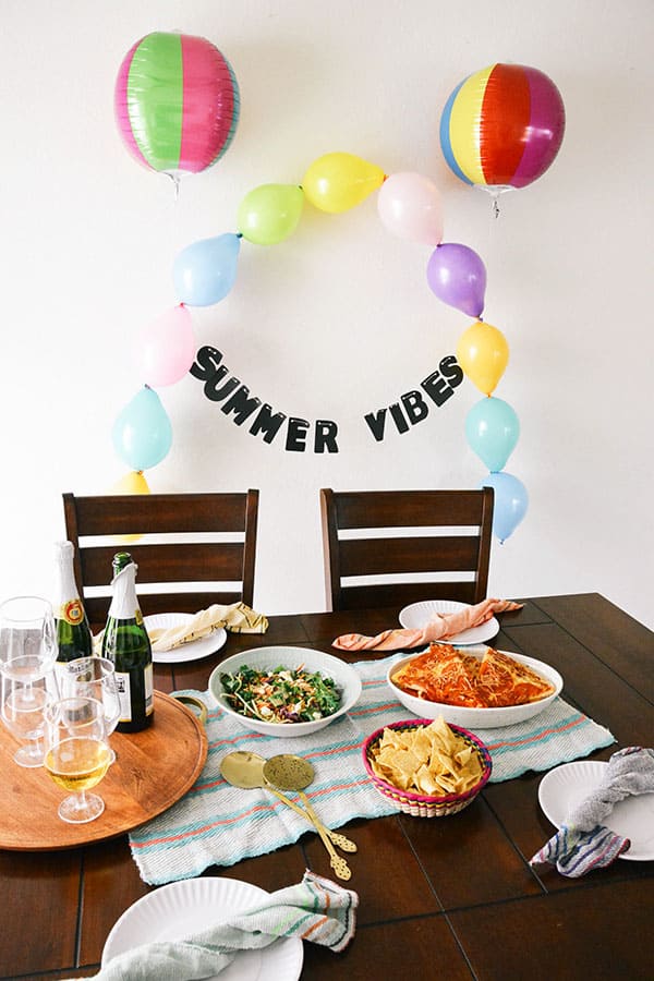 Easy summer party balloon decoration idea with a summer vibes garland behind a table set for a kid's dinner party.