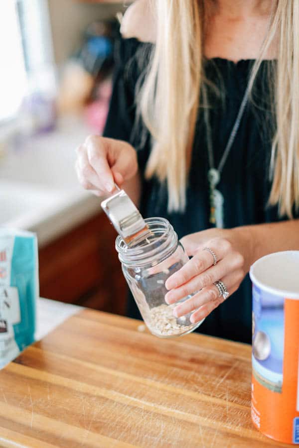 A woman scooping rolled oats into a mason jar.