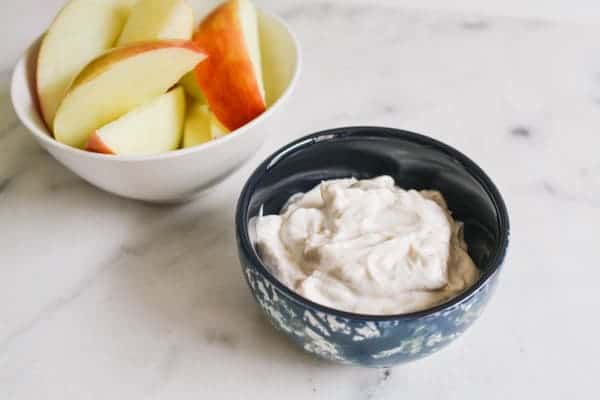 Greek yogurt tip in a blue and black bowl next to a bowl of apple slices.