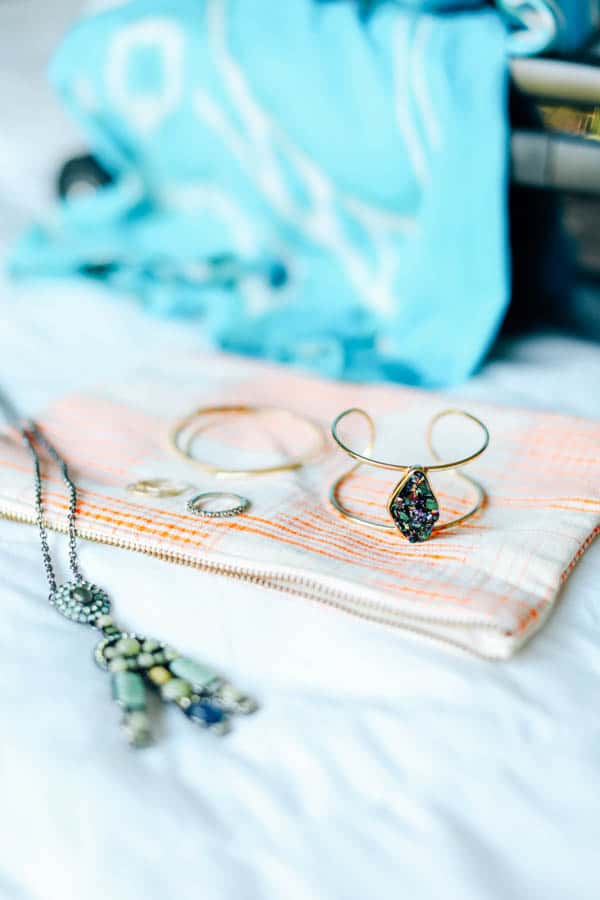 Jewelry on a zippered pouch laying on a bed. 