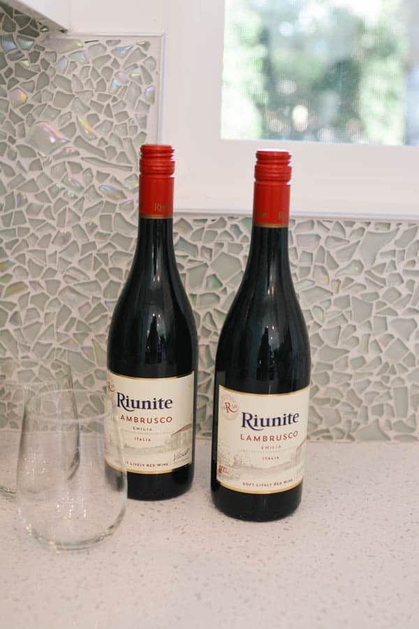 Two bottles of Riunite Lambrusco on a kitchen counter next to stemless wine glasses.