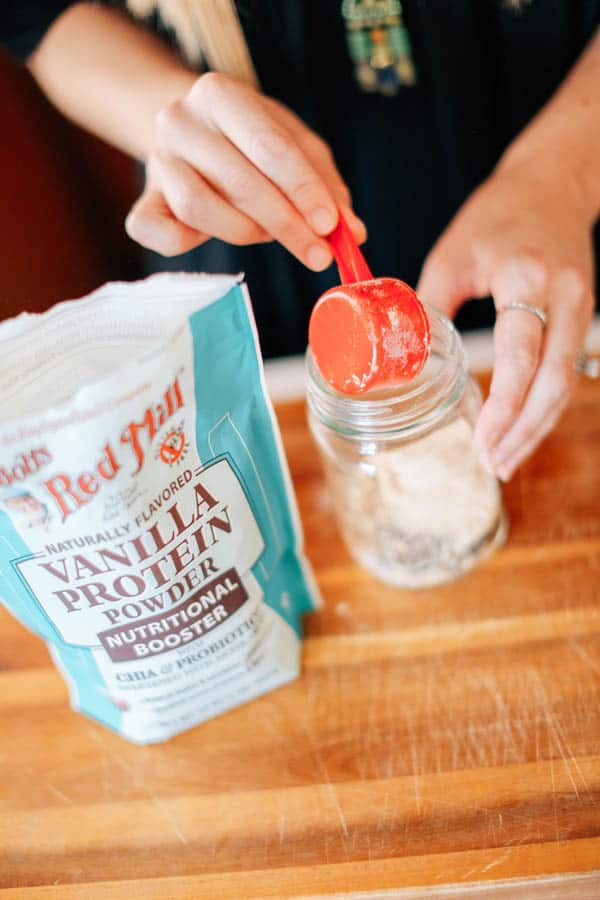 A woman adding vanilla protein powder to overnight oats.