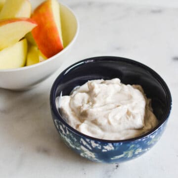 A small bowl of Yogurt Dip for Apples with Greek yogurt, cinnamon and vanilla next to apple slices.