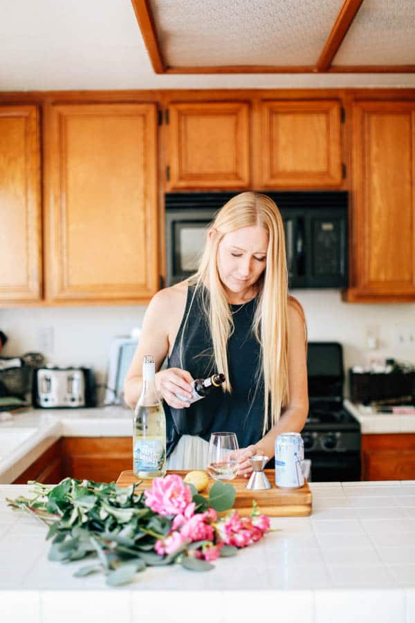 Woman adding bitters to a wine cocktail in a stemless glass on the counter. 