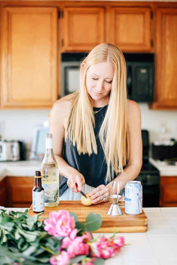 Woman cutting a lemon on a cutting board with cocktail ingredients around her. 