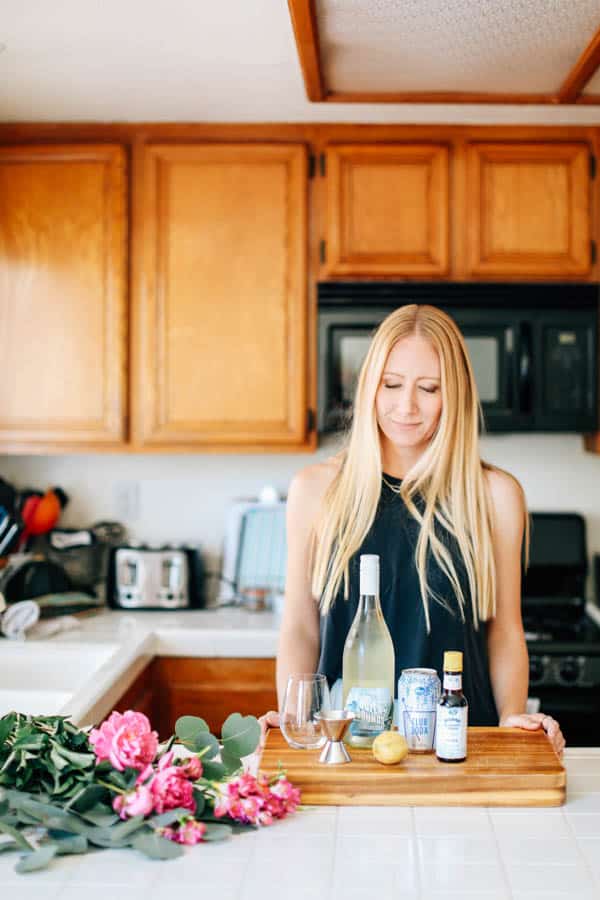 Woman in the kitchen with ingredients to make a simple white wine spritzer cocktail. 