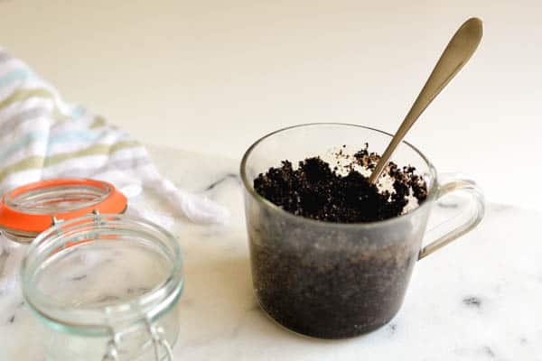 Coffee scrub mixture in a glass mug with a spoon.