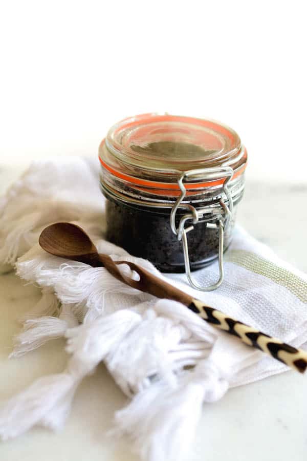 A jar of coffee scrub next to a wooden spoon.