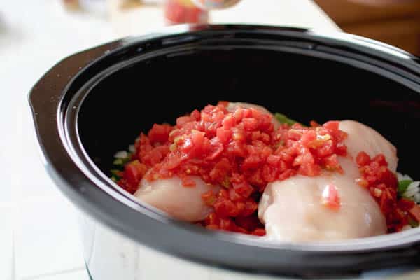 Uncooked chicken breasts topped with tomatoes in a slow cooker. 
