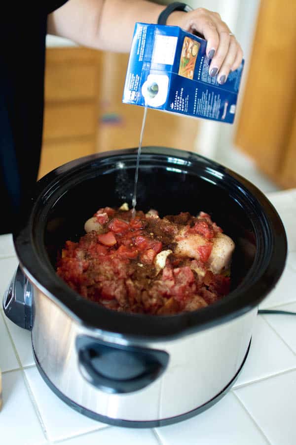 Woman adding chicken stock to soup in the slow cooker. 