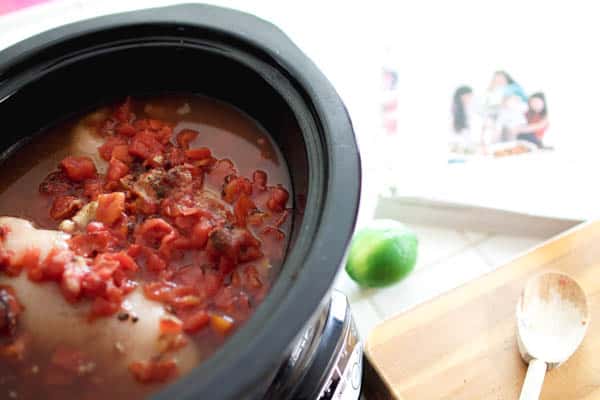 Tomatoes and chicken in a crockpot without a lid next to a spoon and lime. 