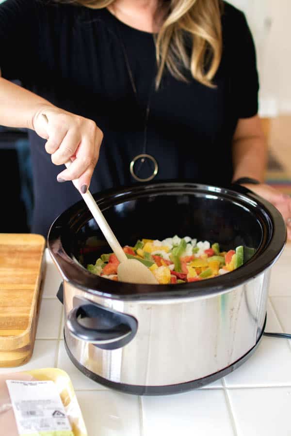 A woman stirring peppers and onions in a slow cooker. 