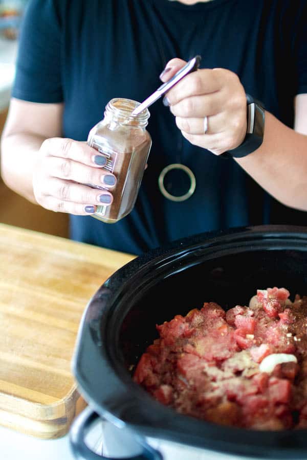 Woman adding spices to a crockpot soup.
