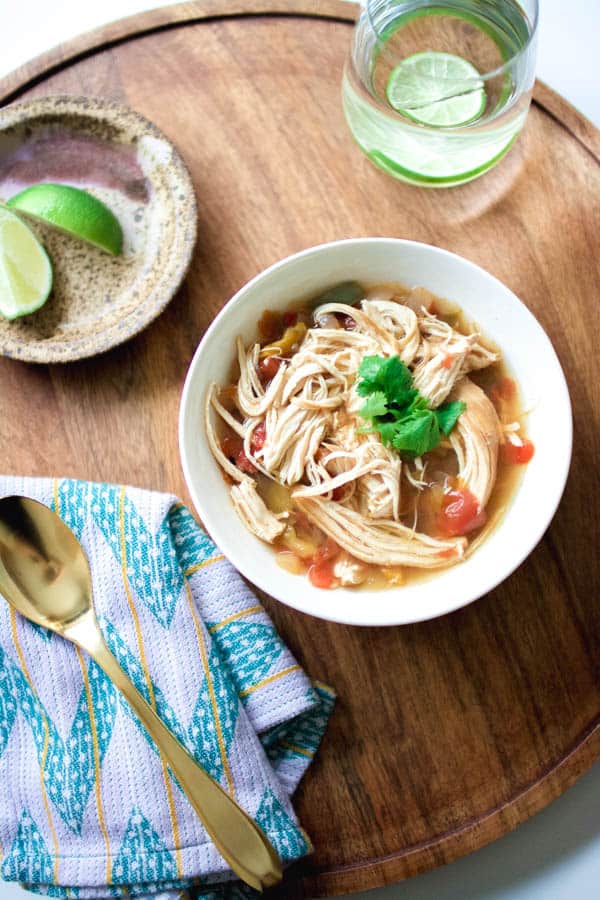 A white bowl with a portion of Chicken Fajita Soup topped with cilantro on a wooden tray. 