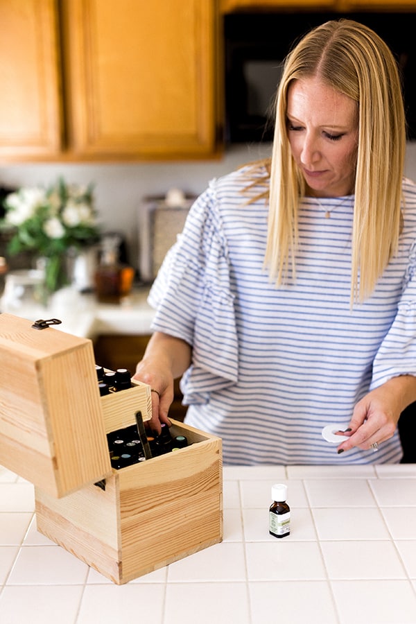 Woman choosing essential oils out of a wooden holder on the counter. 