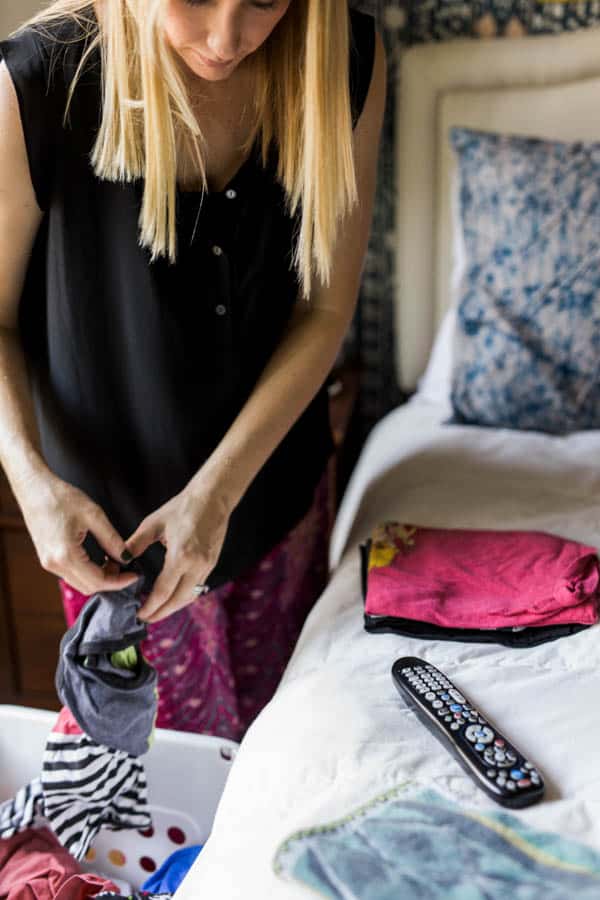 Woman folding laundry with the tv remote on the bed next to folded laundry. 