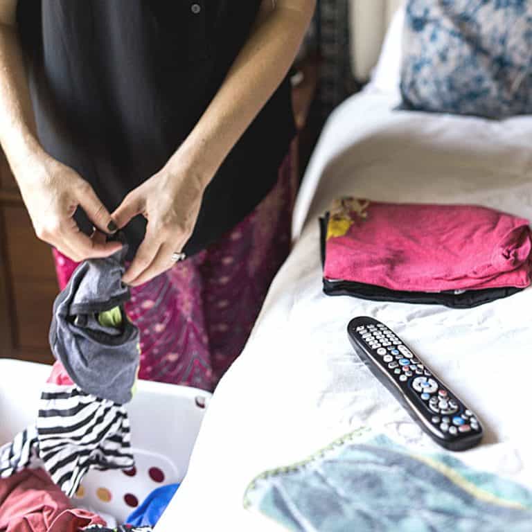 Close up of a mom folding laundry with a TV remote on the bed next to the clothes.