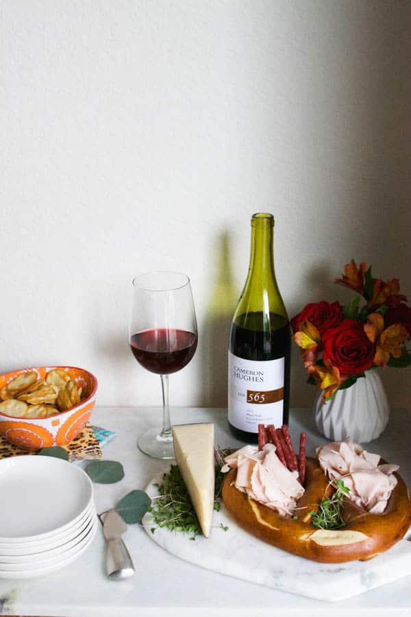 A small wine and cheese platter on a side table with a bottle and glass of wine next to it. 