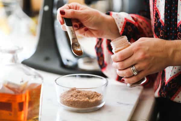 Woman adding some spices to a small bowl of brown sugar.