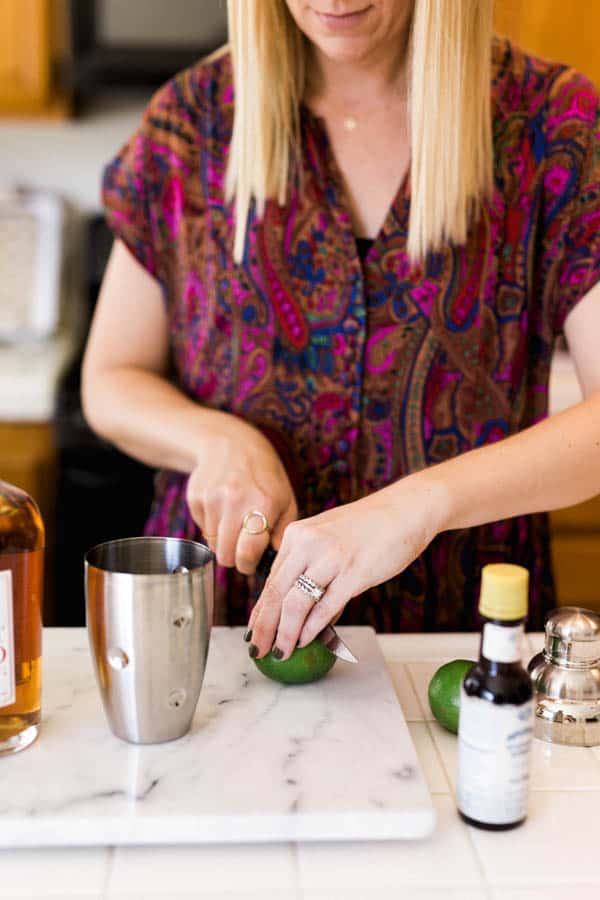 Woman cutting a lime with a knife next to a cocktail shaker. 