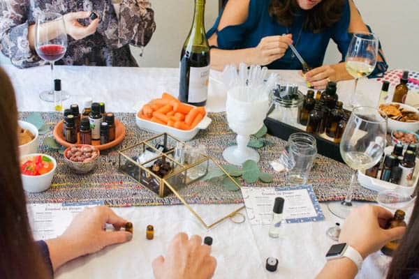 Women gathered around a table mixing essential oils and sipping wine.