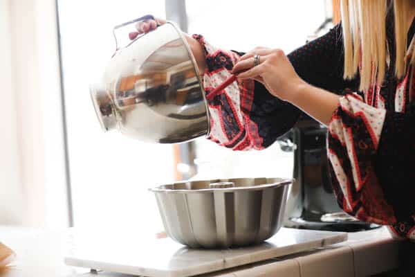 Woman adding cake batter to a bundt pan on a counter.