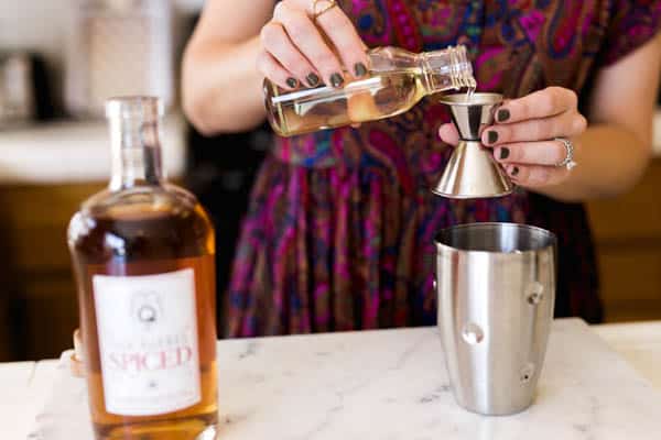 Adding vanilla simple syrup to a jigger above a cocktail shaker. 