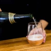 Woman pouring champagne into a glass of kombucha.