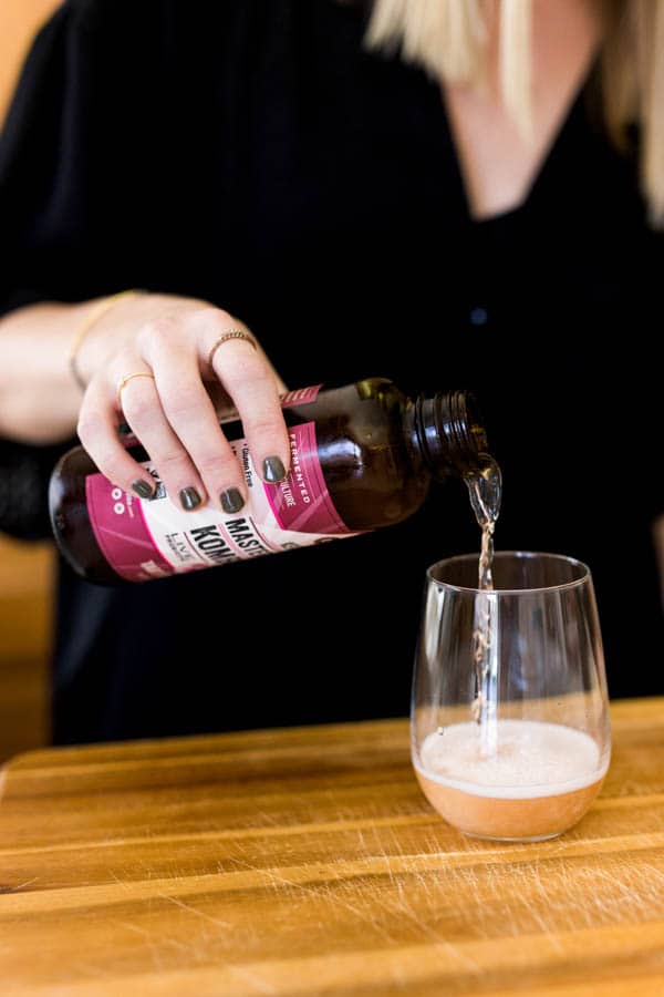 Woman pouring kombucha into a glass.