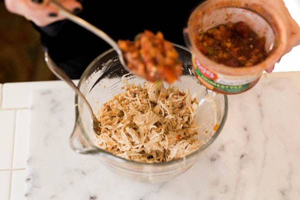 Spooning salsa into a bowl of shredded chicken.