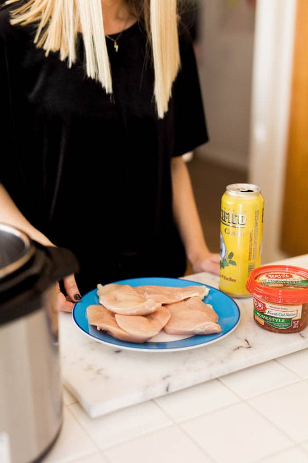 Woman standing next to an instant pot and raw chicken and a can of beer on a counter. 