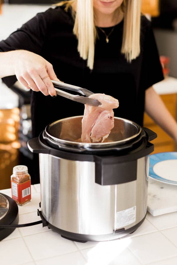 Woman adding raw chicken to an Instant Pot. 