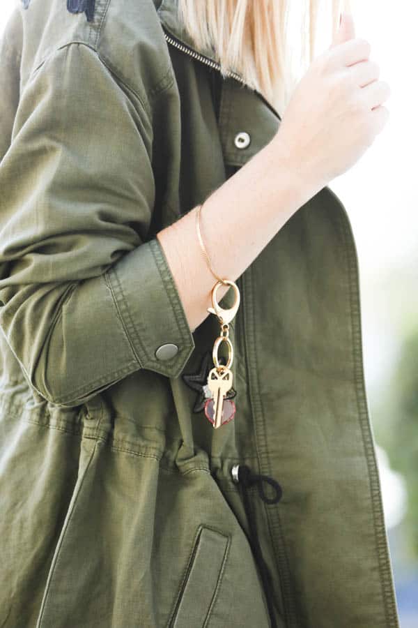 Woman in green jacket wearing a gold bracelet with keys hanging from it.