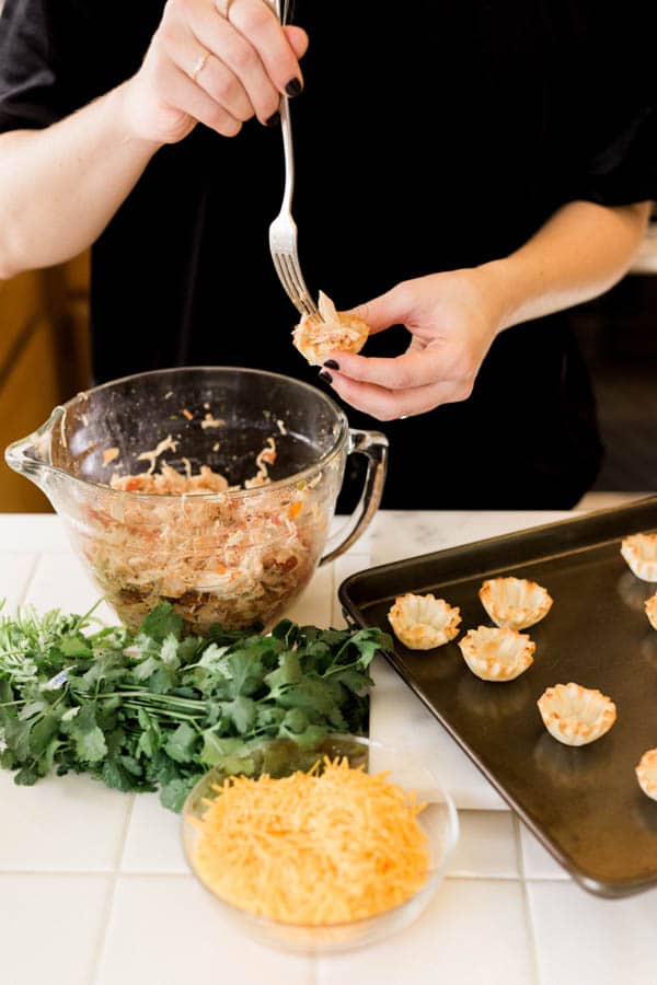 Woman assembling chicken salsa taco cups.