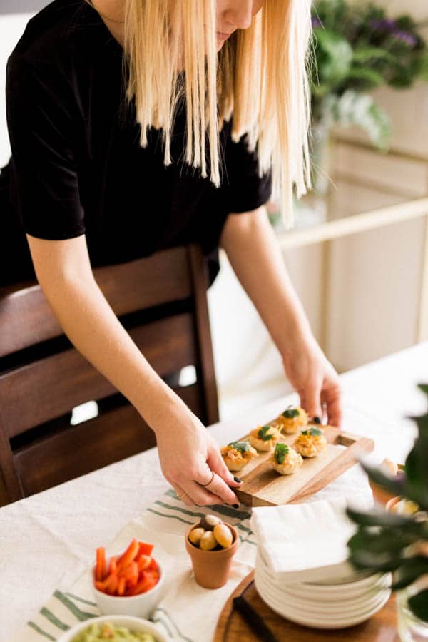 Woman placing a small wooden tray with appetizers on a table for a party. 