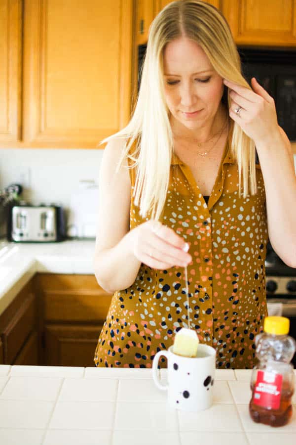 Woman in a sleeveless blouse making tea at the kitchen counter.