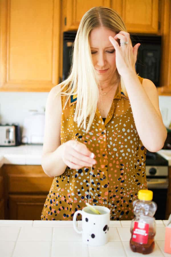 Blond lady in blouse making hot tea at the kitchen counter. 