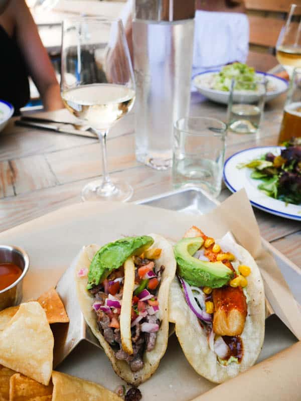 Tacos on a plate with a glass of wine and a friend in the background. 