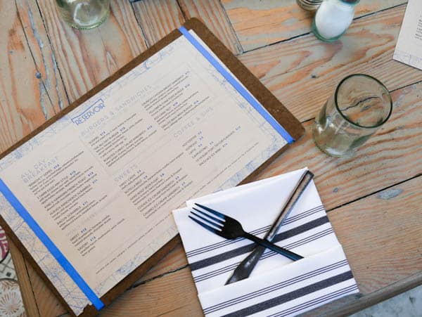 Restaurant menu on a wood table with a napkin and silverware next to it.