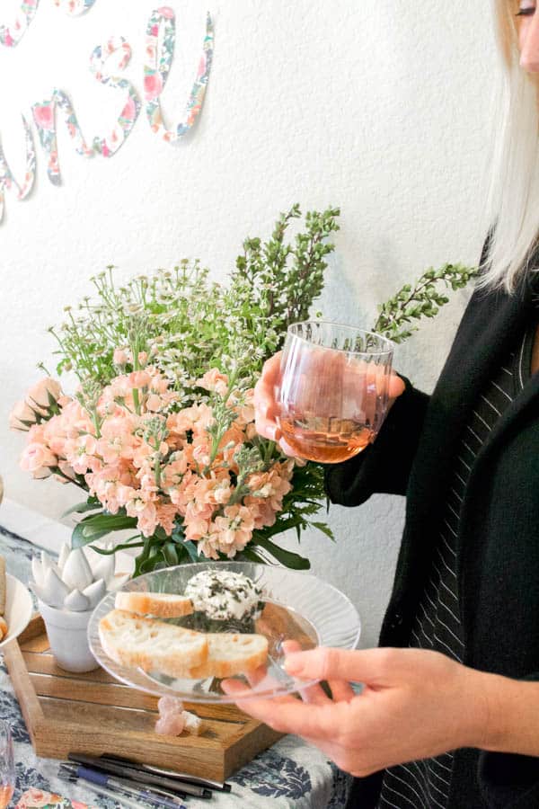 Woman holding a glass of rose and a plate of food.
