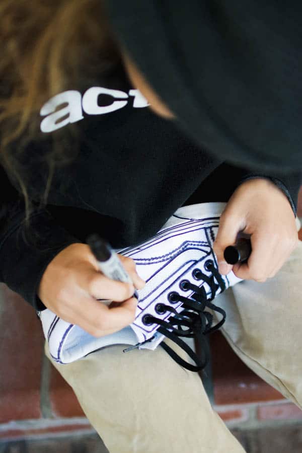 Boy using sharpie to make streetwear Vans sneakers. 