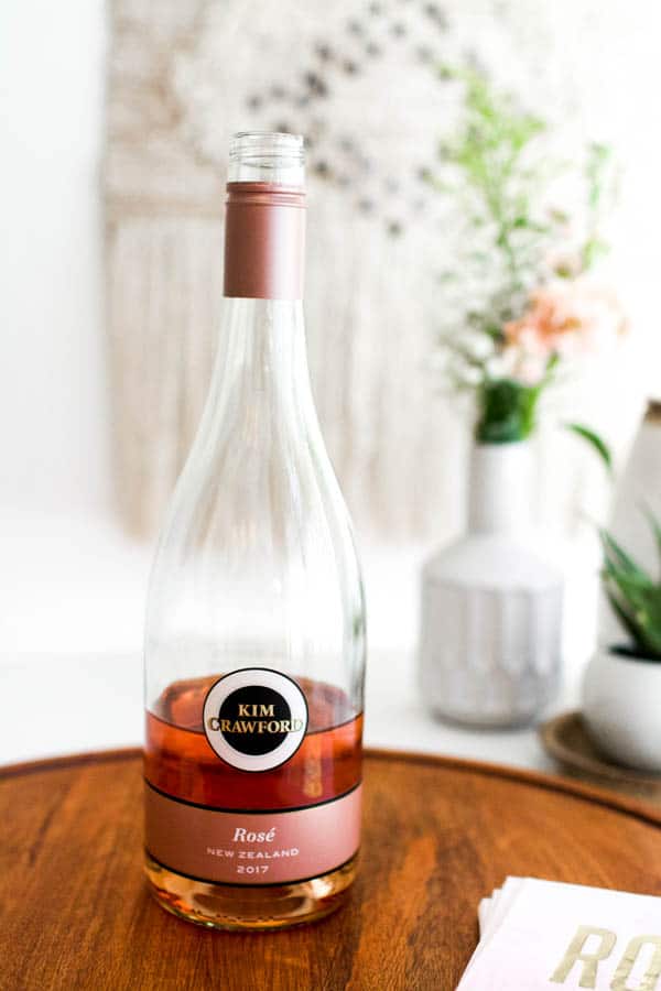A half empty bottle of Kim Crawford rose on a wooden tray on a table. 