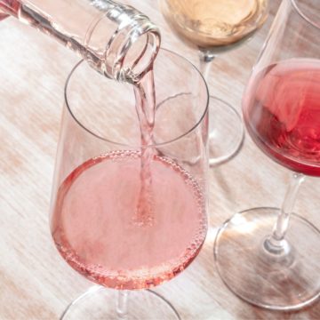 A close up of a wine glass with someone pouring rose into it.