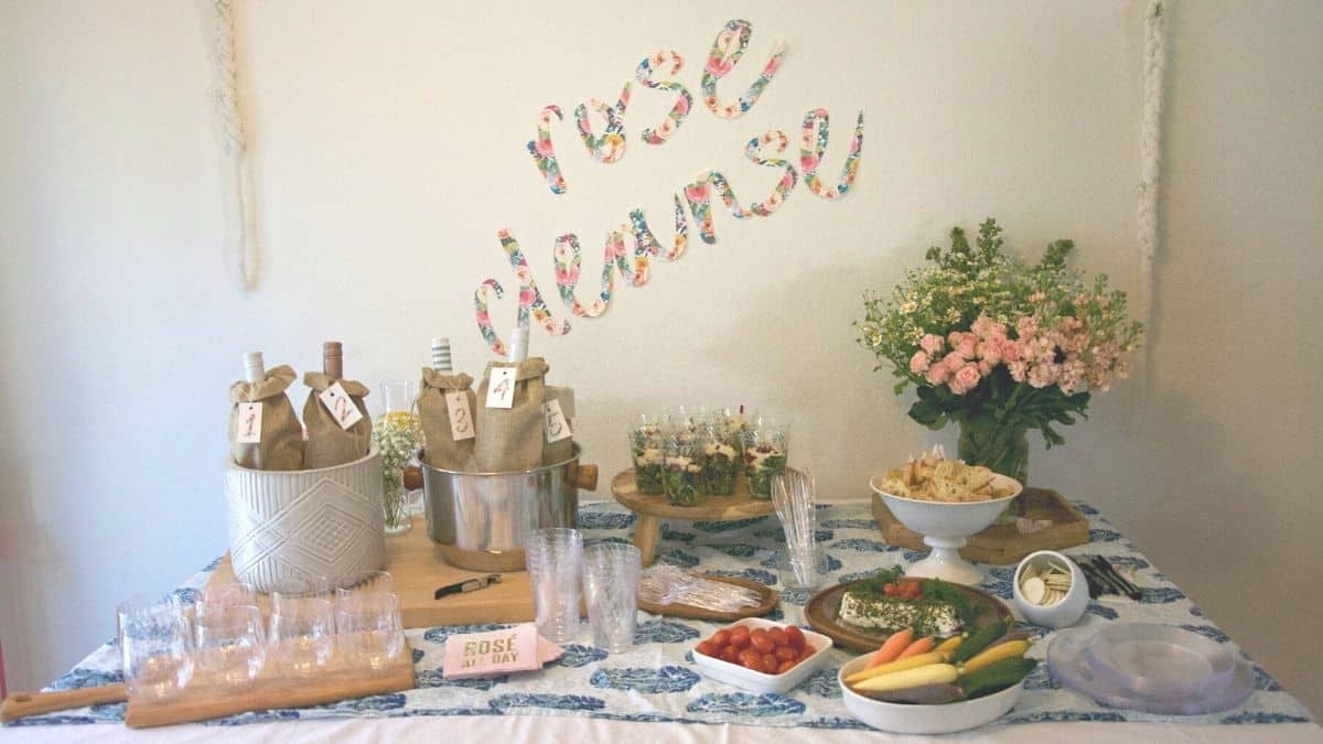 Text- Rosé Cleanse in fabric letters on the wall above a party table for a wine tasting party.