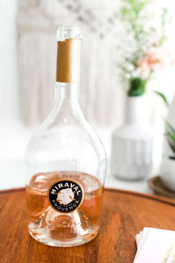 A half full bottle of Miraval rose on a wooden tray on a table. 